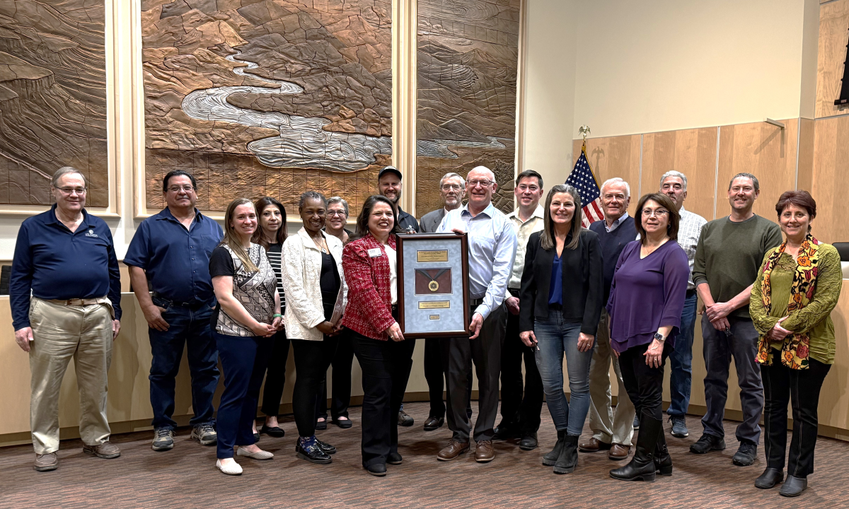 A group of people poses for a photo with a framed medal.