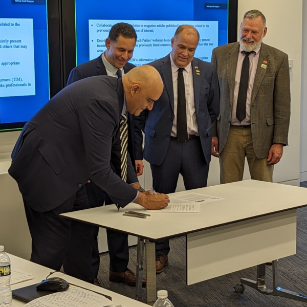 a photo of FHWA Administrator Bhatt signing the 5-year MOA as APWA CEO Scott Grayson, APWA President Gary Losier, and APWA Past-President Keith Pugh observe