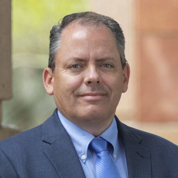 Chris Ewell smiling for a photo in a suit and tie.