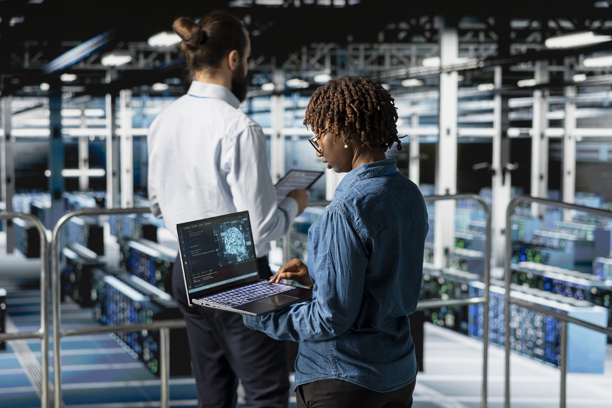 Two individuals stand in a spacious data center, each using an electronic device.