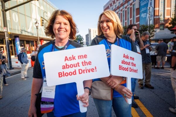 Two women smile and hold signs promoting the PWX blood drive.