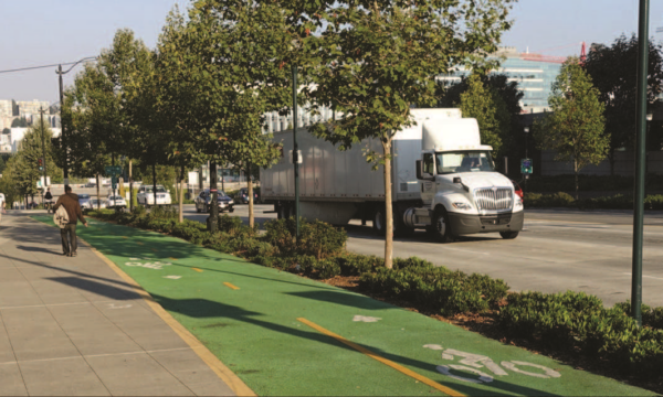 a photo of cars and trucks driving on the road, with bicycle lanes and pedestrians in the foreground