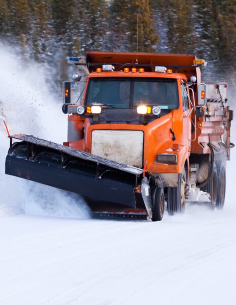 An orange truck with plow clears a road of snow.