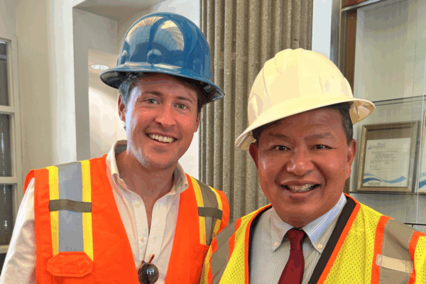 Two men in hard hats and safety vests smile for a photo.
