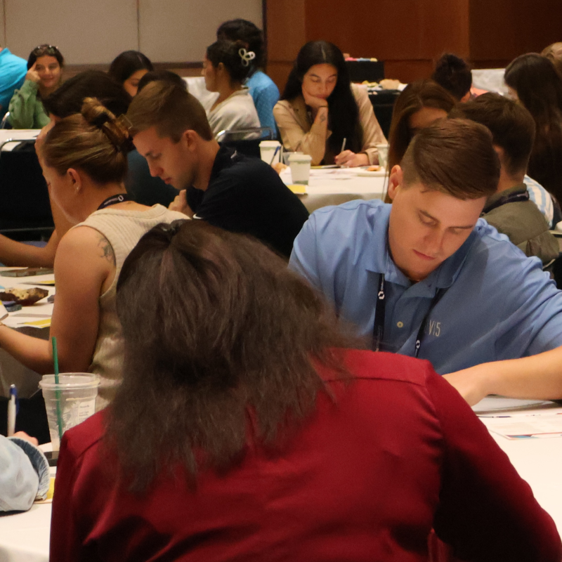 A group of young professionals sits at round tables, deeply focused on writing and discussing during the APWA Young Professionals (YP) Summit.
