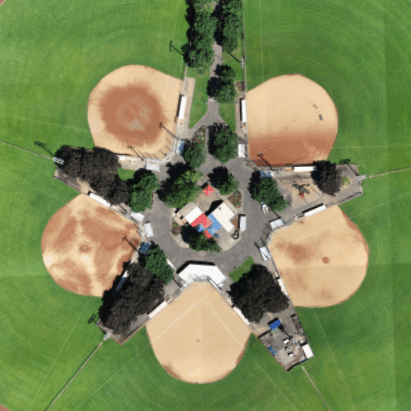 A drone photo of baseball fields, buildings, and trees.