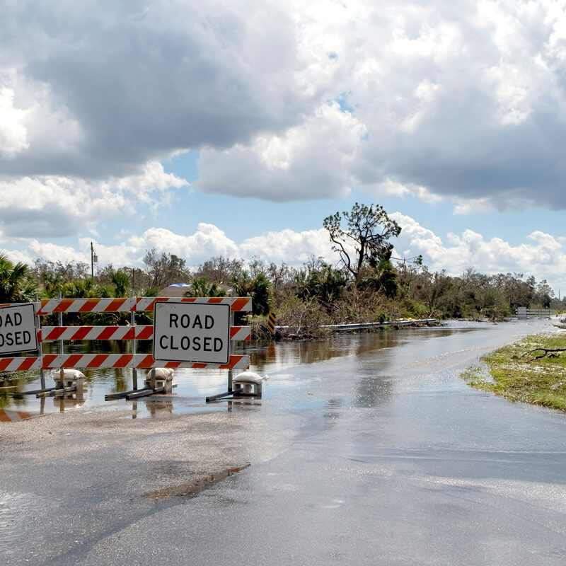 Hurricane flooded street with road closed signs blocking driving of cars. Safety of transportation during natural disaster concept