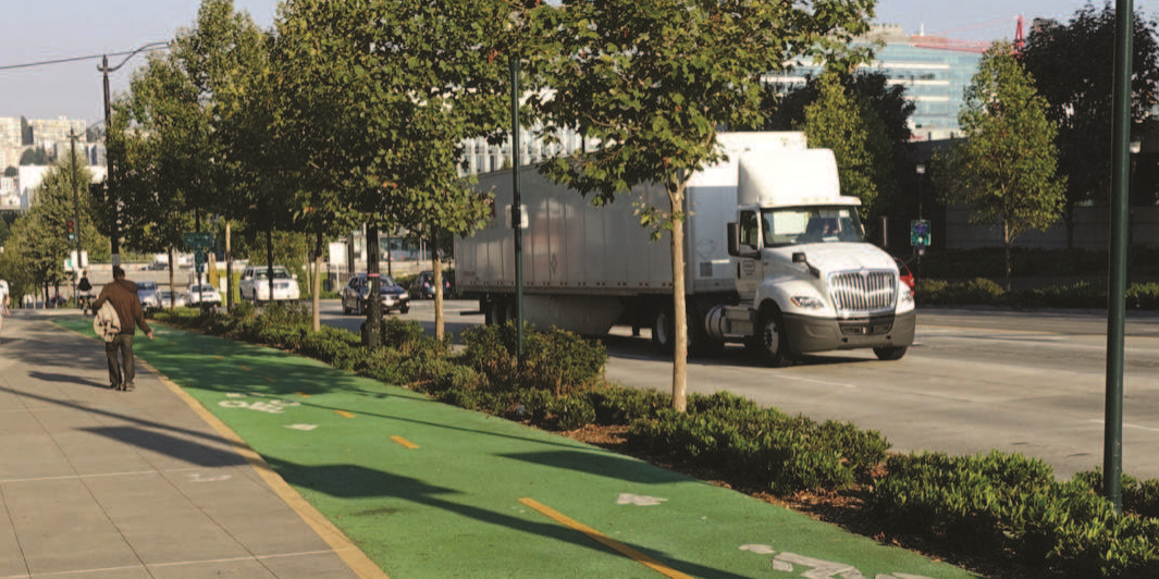 a photo of cars and trucks driving on the road, with bicycle lanes and pedestrians in the foreground