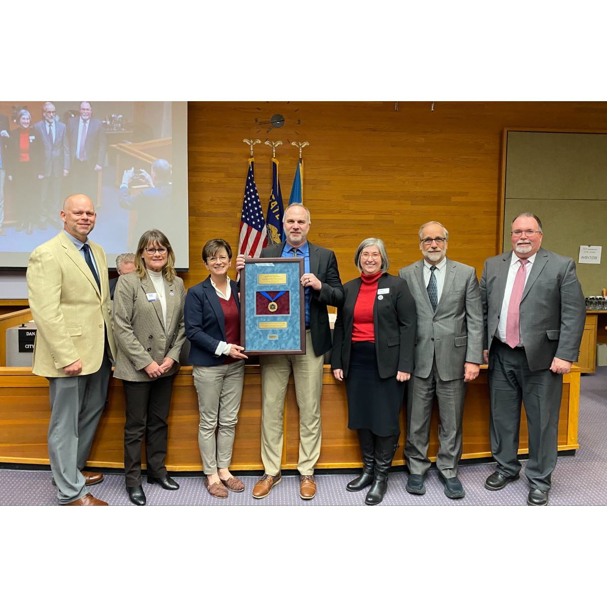 A group of people poses for a photo with a framed medal.