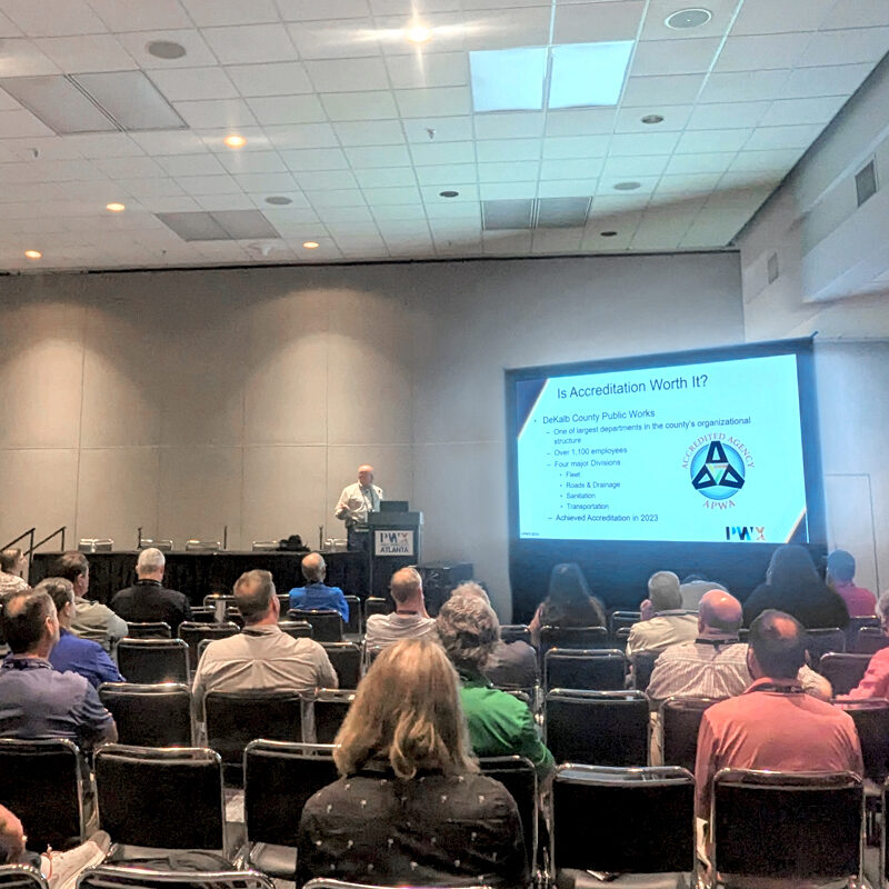 People sit in a convention center room and listen to a speaker present on APWA Accreditation.