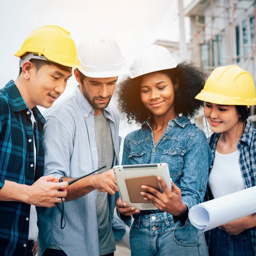 Architector and engineers with draft plan of building and tablet talking on constructing site. Construction manager and engineer working on building site.